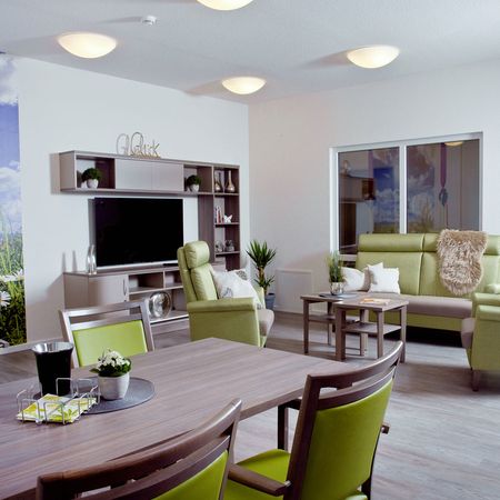 Innenansicht eines Pflegeheims: Wohnzimmer mit einem Tisch und Stühlen, einladend und komfortabel gestaltet.